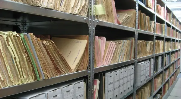 Rzędy półek archiwum wypełnione teczkami i pudłami. Na jednej z teczek widoczna jest sygnatura: "11497/58".