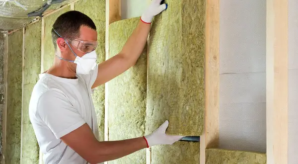 Un ouvrier installe un panneau d'isolation minérale dans une structure murale en bois, respectant les normes d'isolation des murs RT 2020.