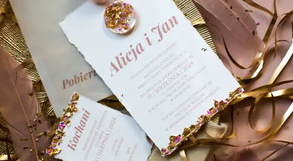 Eleganckie zaproszenia ślubne z piórami i złotymi zdobieniami.