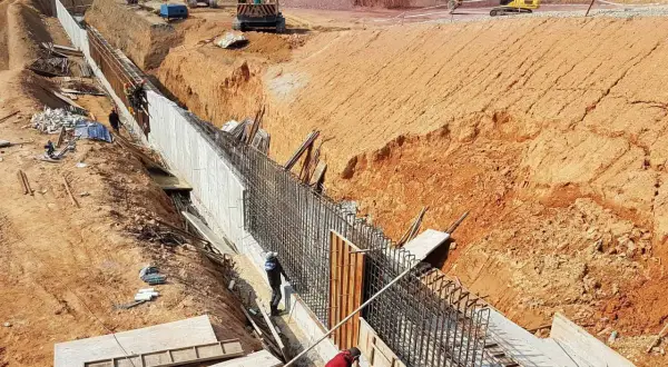Budowa muru oporowego, gdzie pracownicy przygotowują zbrojenie. Widać koparki i wykop. To kluczowy etap, by wiedzieć, ile potrzeba betonu na fundamenty.
