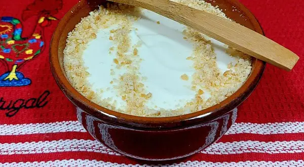 Delicioso serradura portuguesa en cuenco de barro, espolvoreado con galleta triturada y una cuchara de madera.
