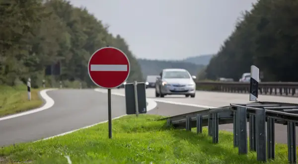 Znak b2, zakaz wjazdu, stoi przy krętej drodze. Samochody jadą w tle.