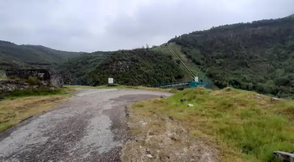 Camino de acceso a la fervenza da roca, con tuberías y vegetación en la ladera.