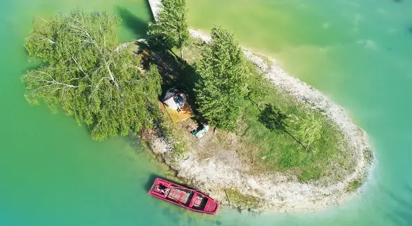 Un séjour insolite en Île-de-France : une petite île avec une cabane, un bateau rouge et un ponton.