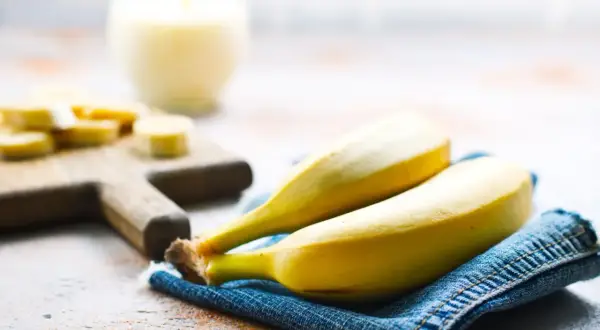 Dwa dojrzałe banany na dżinsowej serwetce, obok pokrojonych bananów i szklanki napoju. Interesuje Cię indeks glikemiczny bananów?
