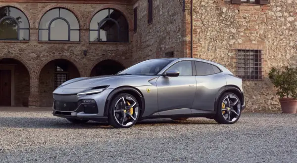 Srebrny Ferrari SUV Purosangue zaparkowany przed kamiennym budynkiem z łukowymi oknami.