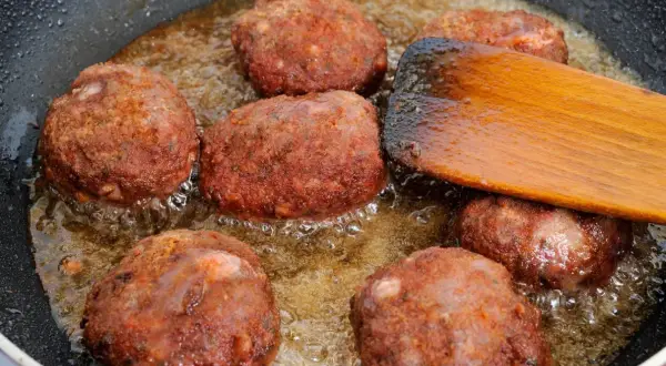 Na patelni smażą się kotlety mielone. Drewniana łopatka pomaga przewracać je, by równomiernie się zarumieniły.