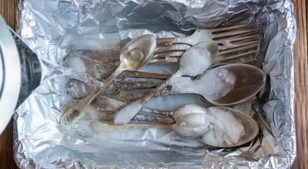 Srebrne sztućce w folii aluminiowej, zalewane wrzątkiem z solą. Prosty sposób, jak wyczyścić srebro w domu.