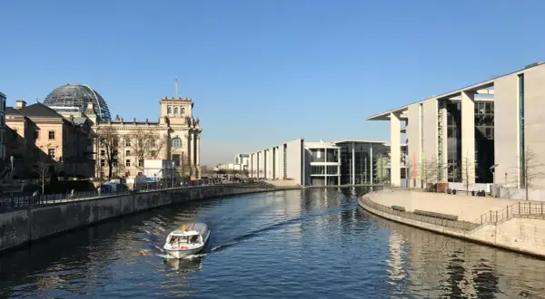 Ein Boot fährt auf der Spree am Reichstagsgebäude und modernen Gebäuden des Regierungsviertels Berlin vorbei.