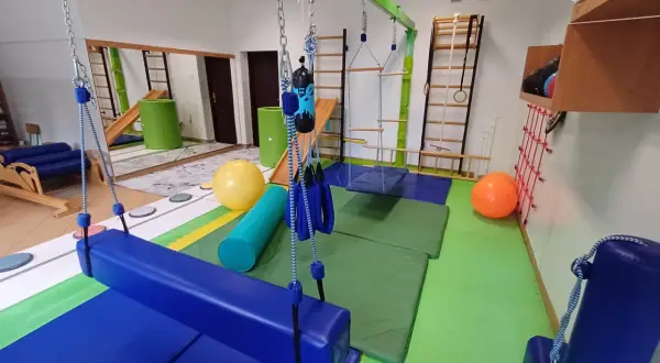 Sala do terapii integracji sensorycznej: huśtawki, drabinki, piłki i materace do ćwiczeń.