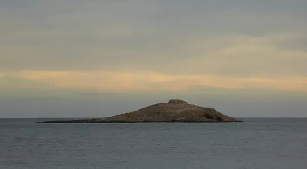 Isla de San Andrés, Almería, un islote rocoso en el mar con gaviotas posadas. Cielo nublado con tonos anaranjados.