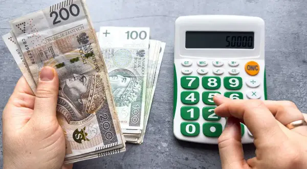 Ręka trzyma banknoty 200 zł i 100 zł, obok kalkulator z wyświetloną kwotą 50000. Czy to już minimalna krajowa?