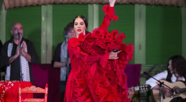 Bailaora de flamenco clásico con vestido rojo voluminoso, castañuelas en mano, acompañada por guitarrista y cantaor.