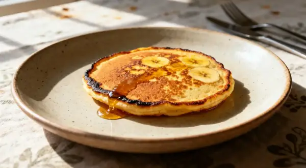 Un délice matinal : des pancakes à la banane dorés, nappés de sirop, sur une assiette en céramique.