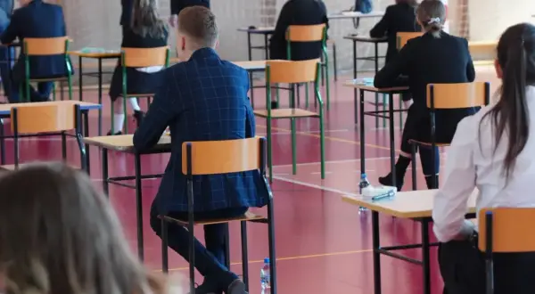 Uczniowie siedzą w ławkach na sali gimnastycznej, skupieni na zadaniach. To moment, kiedy sa matury, a przyszłość wielu zależy od tych egzaminów.
