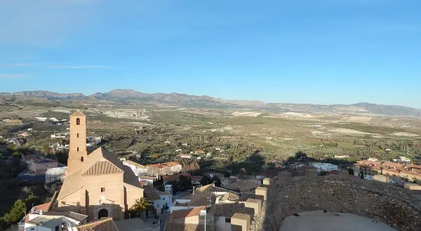 Vistas de Serón que ver: iglesia con campanario, tejados y paisaje rural montañoso bajo un cielo azul.
