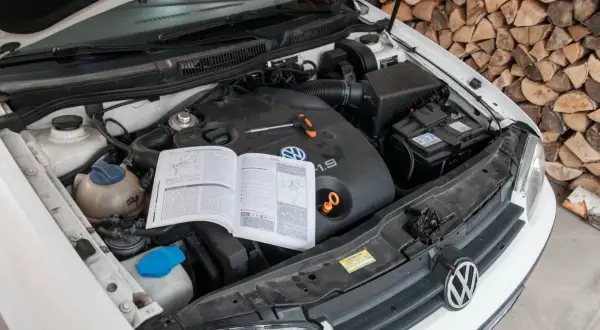 Otwarta maska samochodu z widocznym silnikiem 1.9 TDI, instrukcją obsługi i narzędziami.