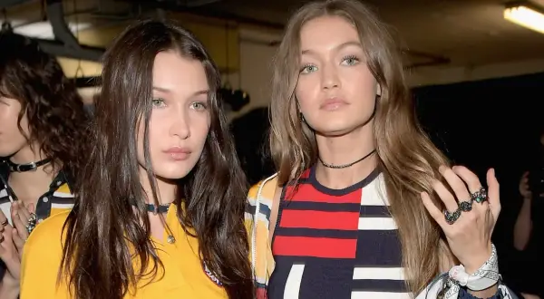 Bella Hadid i Gigi Hadid, siostry i modelki, w modnych stylizacjach. Bella ma ciemne włosy, Gigi jasne. Ich wiek jest nieistotny wobec ich talentu.