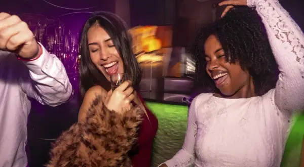 Zwei Frauen tanzen ausgelassen auf einer flinta party hamburg. Sie lachen und halten Gläser in der Hand.
