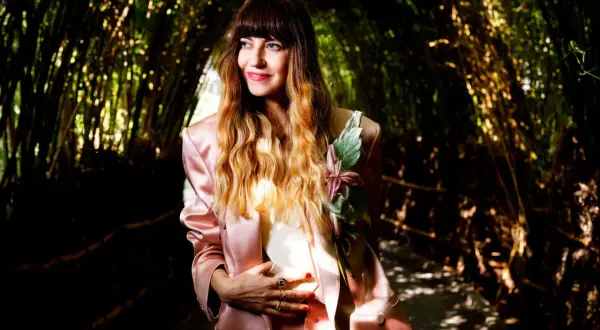 Chiara Tagliaferri, con un tailleur rosa e un fiore sul petto, posa in un tunnel di bambù illuminato dal sole.