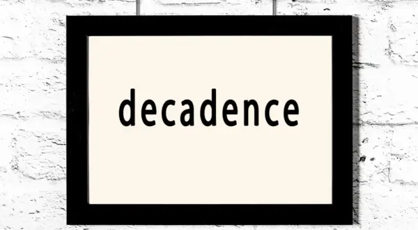 Czarno-biały obraz z napisem "decadence" na jasnym tle, wiszący na białej ceglanej ścianie. To pytanie: co to dekadentyzm?