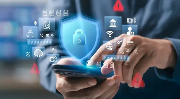 Dłonie trzymające smartfon, na którym wyświetla się tarcza z kłódką, symbole bezpieczeństwa i ostrzeżenia. Potwierdzenie autoryzacji.