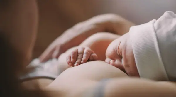 Czułe chwile karmienia piersią. Dziecko ulewa mimo odbicia, ale mama czule je przytula.