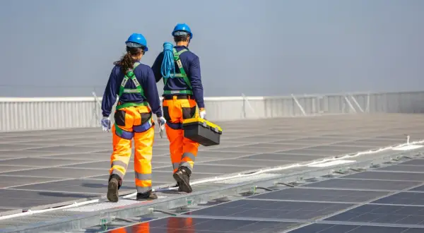 Zwei Techniker in Schutzkleidung gehen über eine Photovoltaikanlage. Regelmäßige Wartung der Photovoltaikanlage ist Pflicht für optimale Leistung.