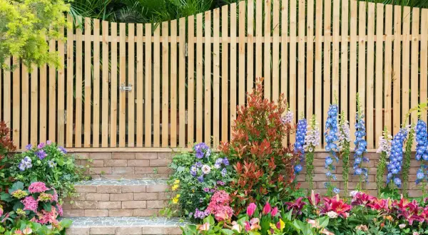 Holz-Gartenzaun-Ideen: Ein schmaler Holzzaun mit Tor, flankiert von bunten Blumen und Ziegelstufen, schafft einen charmanten Eingang.