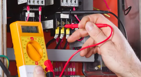 Elektromonter z multimetrem sprawdza instalację elektryczną. To praca wymagająca precyzji, zgodna z zawodem elektromonter kod 311101.