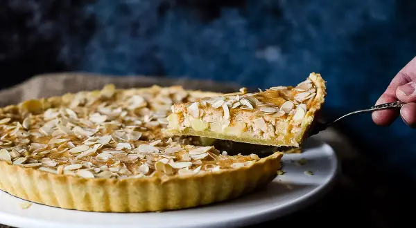 Ein Stück einer sensationellen Apfeltarte mit Mandelblättchen wird herausgehoben. Ein wahrer Genuss!
