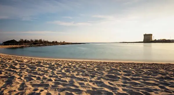 Spiagge Salento Ionico: sabbia dorata, mare calmo e una torre antica all'orizzonte, un sogno ad occhi aperti.