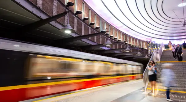 Nowoczesna stacja metra, do której jeździ metro. Pociąg mija peron, a ludzie schodzą po schodach.