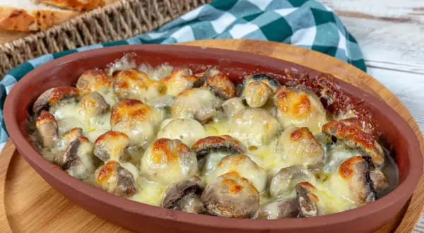 Gorące, zapieczone pieczarki z piekarnika, skąpane w ciągnącym się serze, podane w glinianym naczyniu.