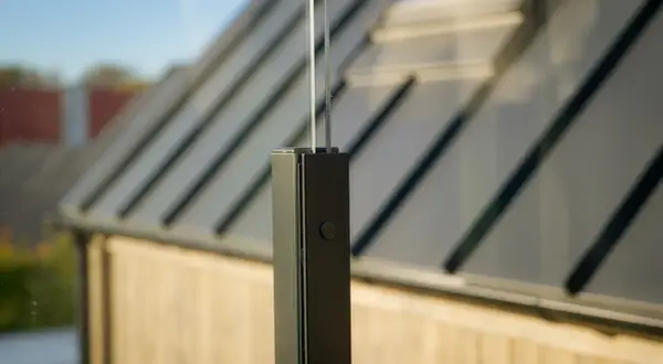 Detaljbild av ett fäste för att montera vindskydd. Glaspanelen är infälld i en svart stolpe.