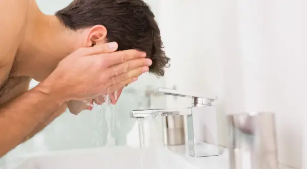 Mann wäscht sein Gesicht mit kaltem Wasser. Er hält seine Hände unter den Wasserhahn, um das Gesicht zu erfrischen.