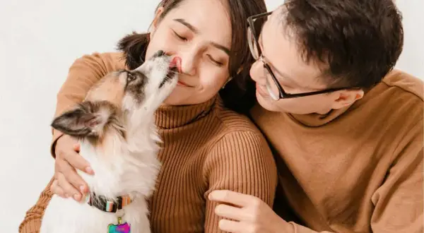 Un tierno momento familiar: un perro lame la nariz de su dueña mientras su pareja lo abraza.