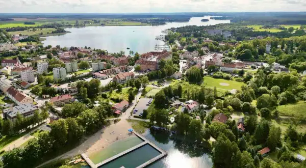 Widok na Ryn z lotu ptaka. Widać jezioro, miasto, plażę i basen. To świetne miejsce na wakacje, pełne atrakcji dla dzieci.