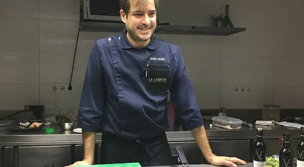 Javier Muñoz chef sonríe en la cocina, con su uniforme azul y el logo de "La Carbona".