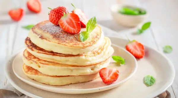 Pancakes soffici con fragole e menta, una deliziosa colazione proteica dolce per iniziare la giornata con energia.