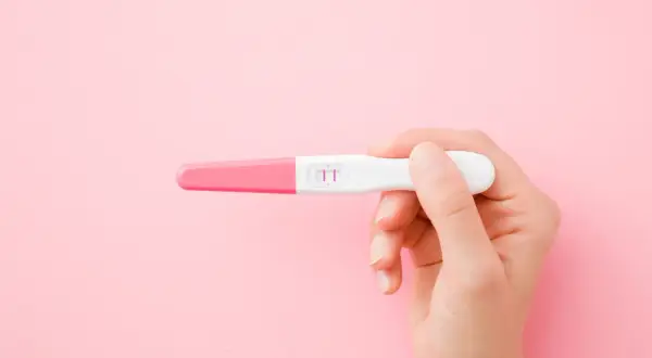 Dłoń trzyma test ciążowy z dwoma różowymi kreskami. To może być początek nowej drogi, nawet jeśli ciąża w młodym wieku niesie wyzwania.