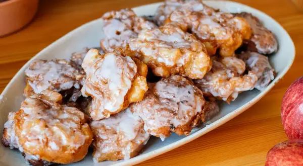 Leckere Apfelkrapfen in der Pfanne, goldbraun gebacken und mit Zuckerguss überzogen, liegen auf einem Teller.