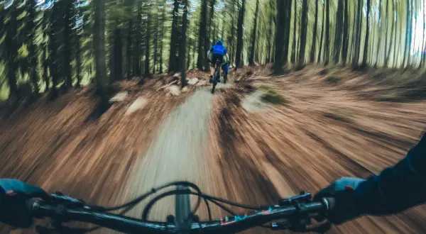 Zjazd rowerowy po leśnym single track glacensis. Widok z perspektywy kierownicy, przed nami inny rowerzysta.