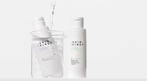 Due flaconi di tonico viso Skin First, uno immerso in un becher con acqua e bollicine, l'altro in piedi.