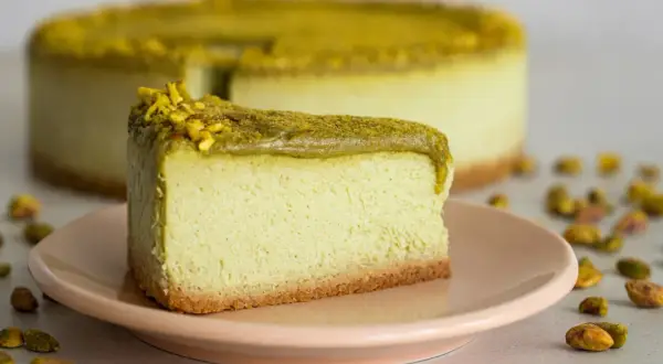 En krämig pistage cheesecake med en krispig botten, toppad med hackade pistagenötter.