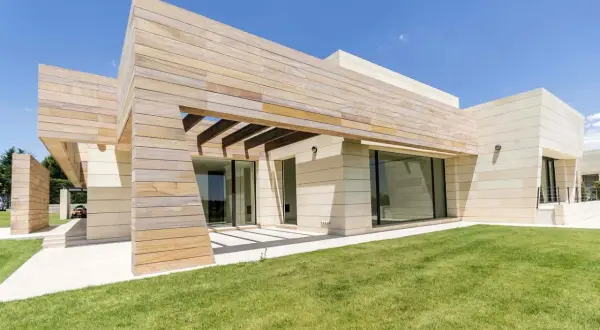 Moderna finca en Madrid con fachada de piedra y madera, césped verde y cielo azul.