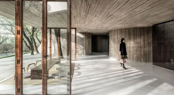 Interior moderno con paredes y techos de hormigón texturizado. Una mujer camina por los suelos de hormigón pulido, proyectando sombras.