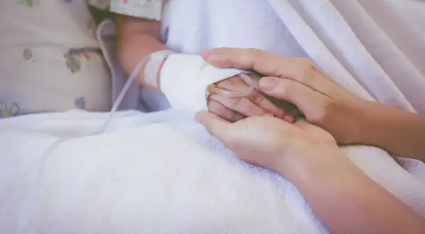 Dłoń rodzica obejmuje dłoń dziecka z wenflonem, symbol wsparcia podczas chemioterapii indukcyjnej.