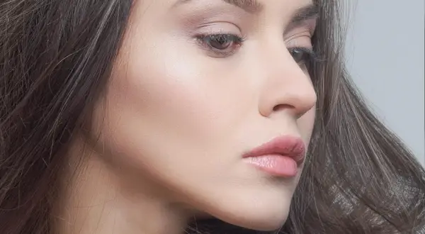 Delikatna twarz kobiety z subtelnym błyskiem na skórze. Makijaż jest tak naturalny, że wygląda jak make up no make up.