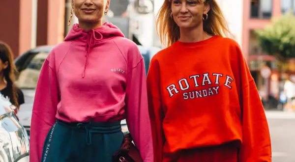 Dwie kobiety w sportowych stylizacjach, idealnych na podróż. Różowa bluza i granatowe dresy lub pomarańczowa bluza i czerwone dresy to świetny pomysł, jak ubrać się do samolotu.